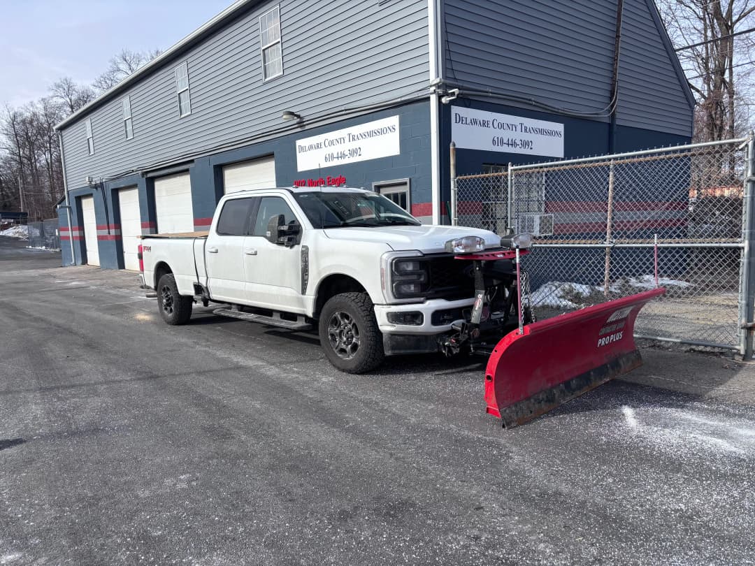Ford truck with a snow plow parked outside a service garage in winter.