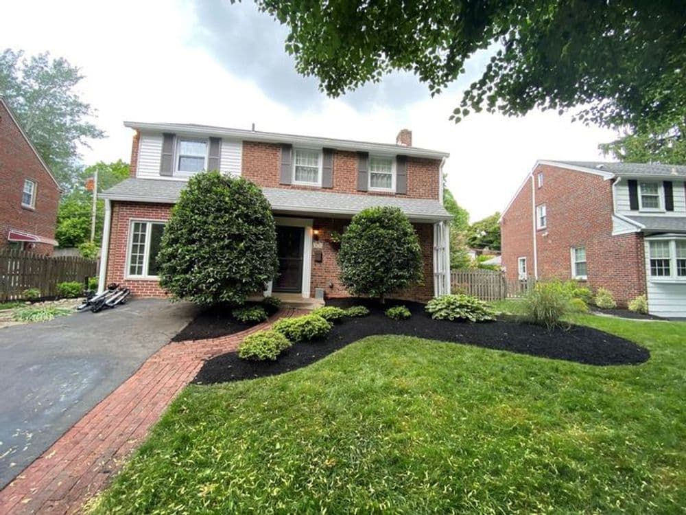Brick house with landscaped front yard and shrubs, featuring a pathway and stormy sky.