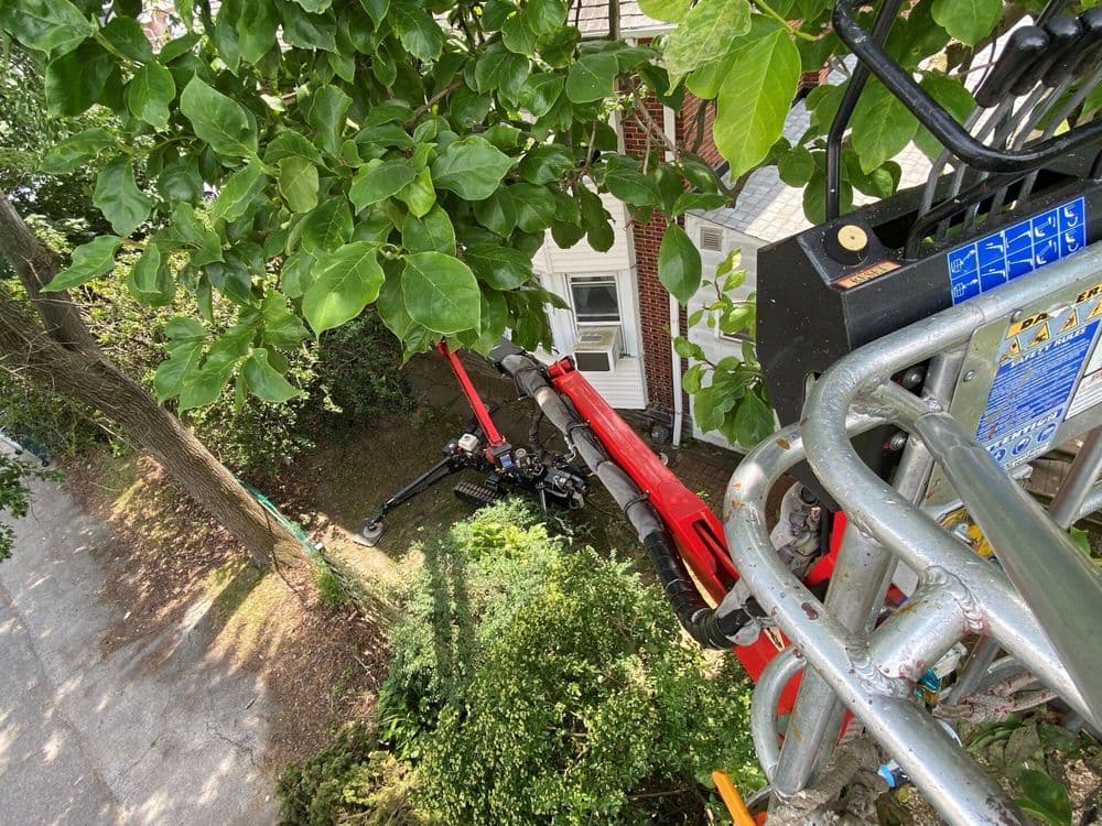 Aerial view of a landscaping lift with a robotic arm, surrounded by greenery and a house.