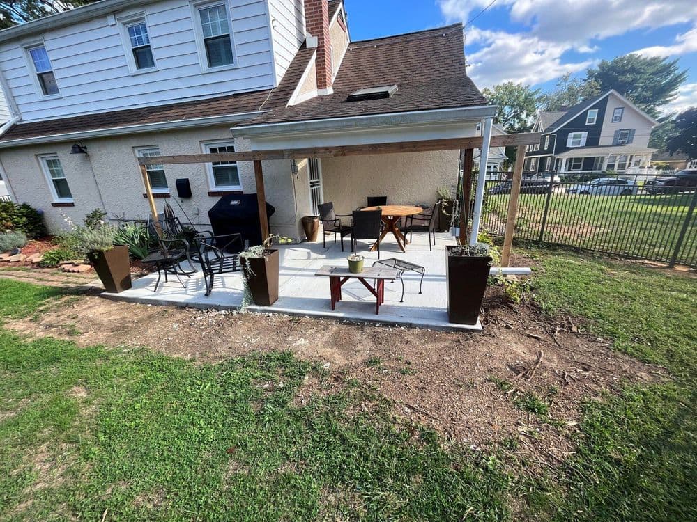 Patio with outdoor seating, dining table, and planters near a house and fenced yard.